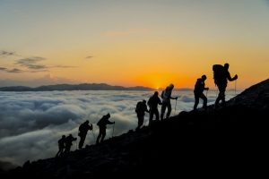 Silhouettes of hikers climbing the mountain at sunset as a metaphor for employee activation